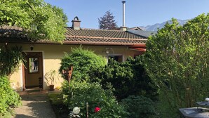 A house with a tiled roof, a chimney, and a garden with various plants and a pathway leading to the entrance. - Quiet vacation apartment, 29sqm, terrace with beautiful garden (Bad Reichenhall)