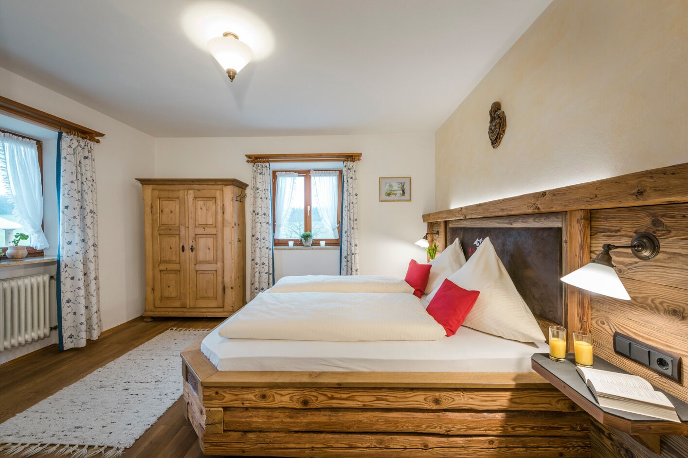Een slaapkamer met een houten bed, nachtkastje met een lamp, een houten garderobe en een raam met gordijnen.