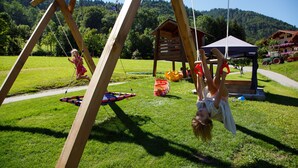 A wooden swing set in a grassy area with a wooden structure in the background.