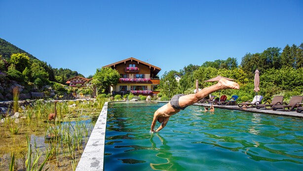A swimming pool with a person diving into it, surrounded by lounge chairs and a building with balconies.