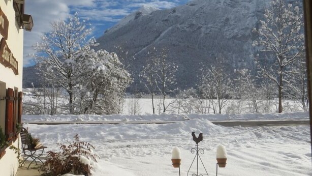 A snowy landscape with a mountain in the background, a bench, and a decorative rooster.