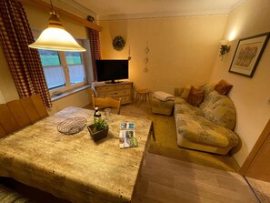 A cozy living room with a wooden dining table, a sofa, a television, and a small side table.