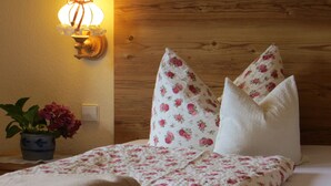 A bedroom with a wooden headboard, floral bedding, a bedside lamp, and a vase with flowers.