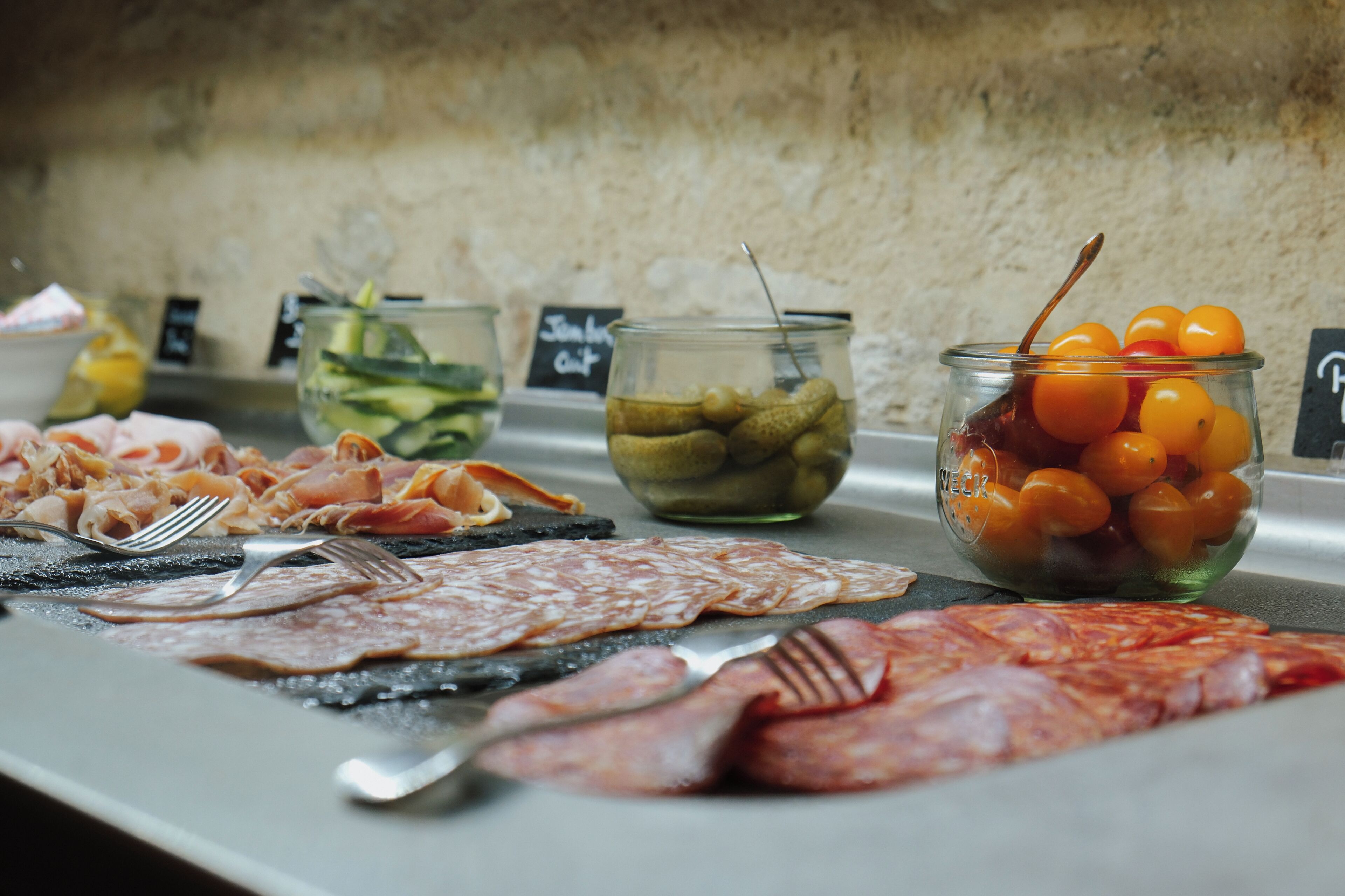 A buffet table with various food items including meats, pickles, and a bowl of cherry tomatoes.