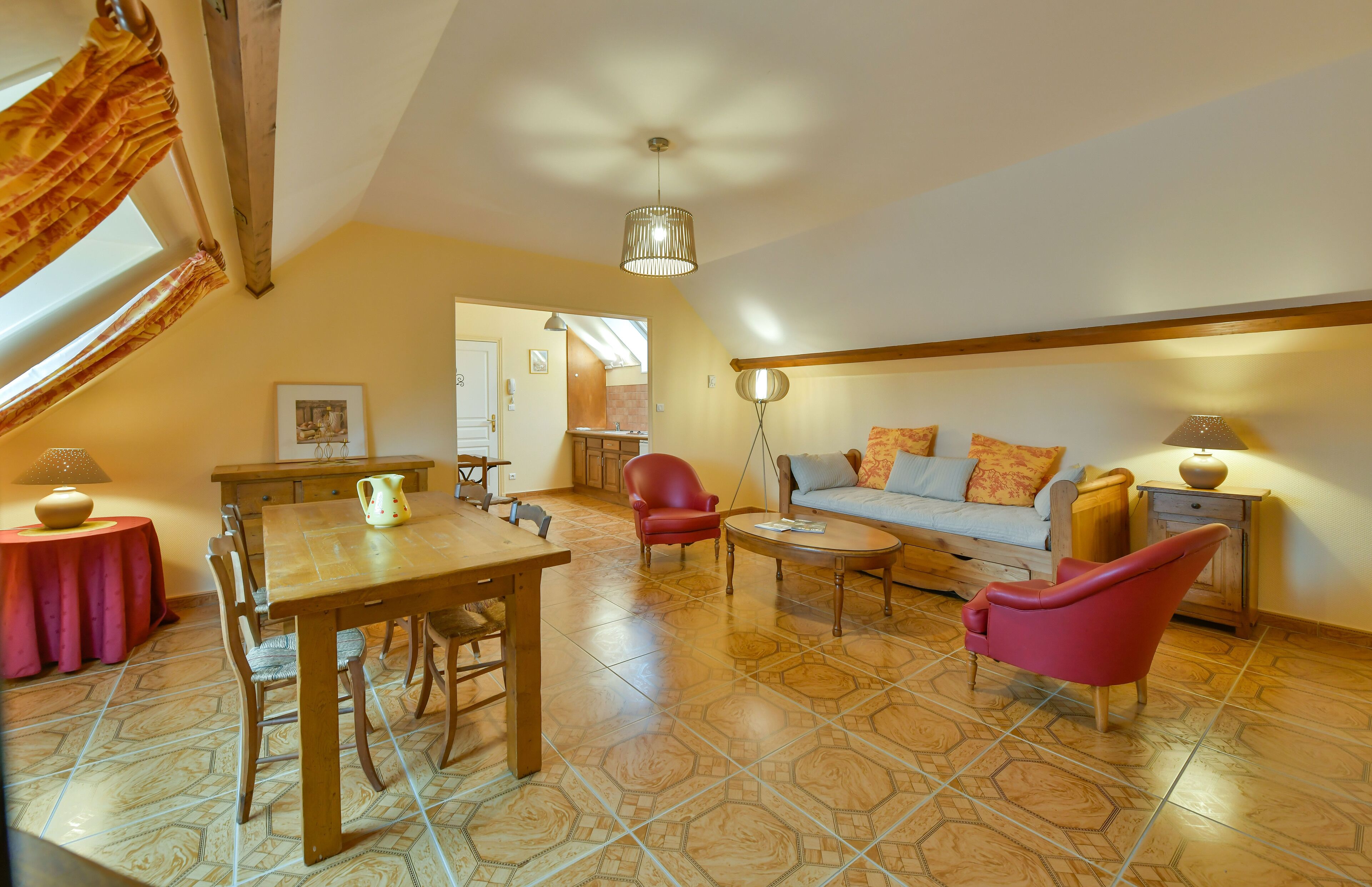 A cozy living room with a wooden dining table, red armchairs, a sofa with cushions, and a floor lamp.