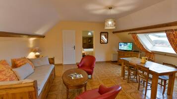 A cozy living room with a sofa, red chairs, a wooden dining table, and a television.