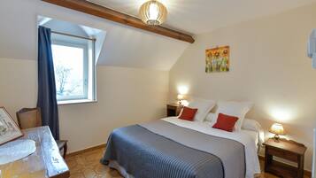 Une chambre à coucher avec un lit, des tables de chevet, une fenêtre avec des rideaux, un tableau au mur et une poutre en bois au plafond.