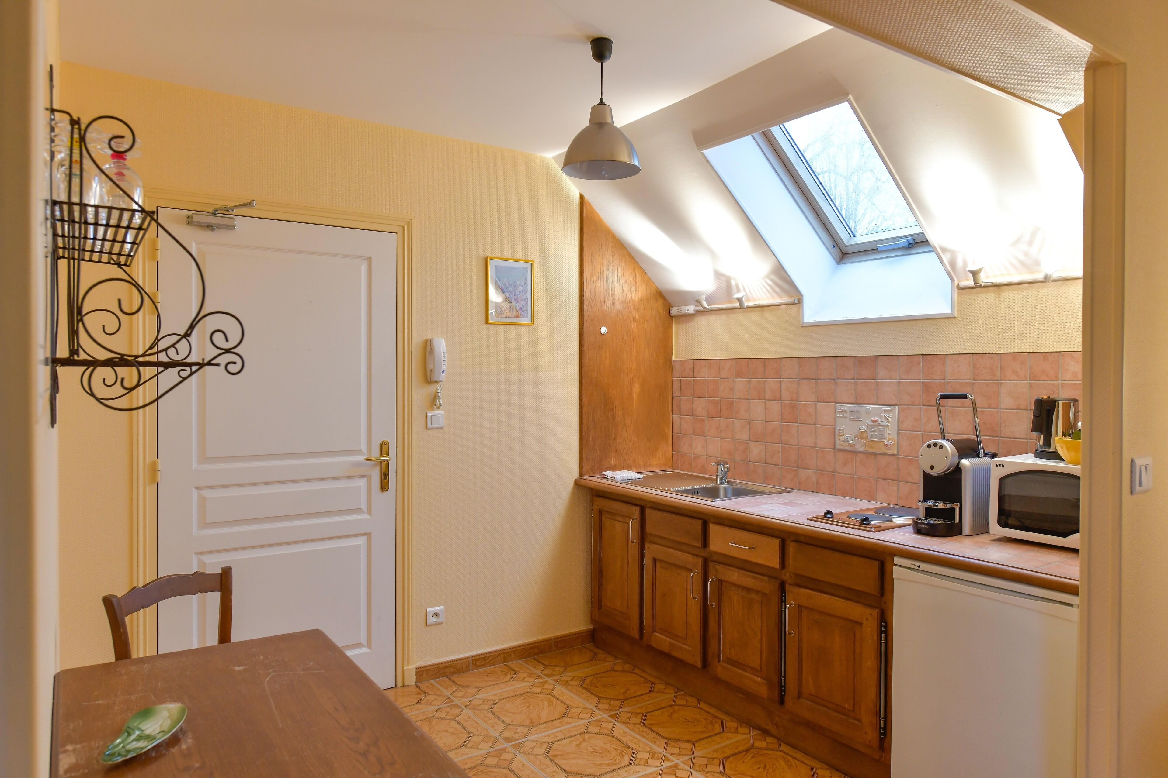 A kitchen with wooden cabinets, a sink, a microwave, and a window with a skylight.