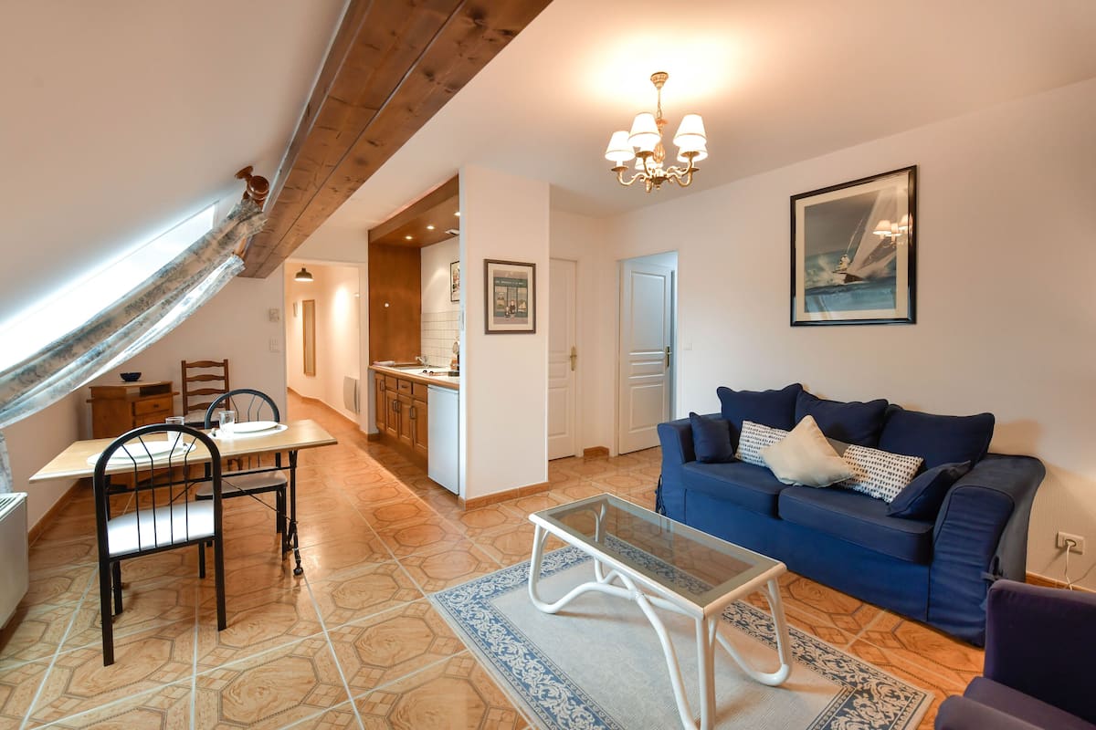 A living room with a blue sofa, a glass coffee table, and a dining area with a wooden table and chairs.