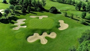 Vue aérienne d’un parcours de golf avec des bunkers de sable et des arbres.