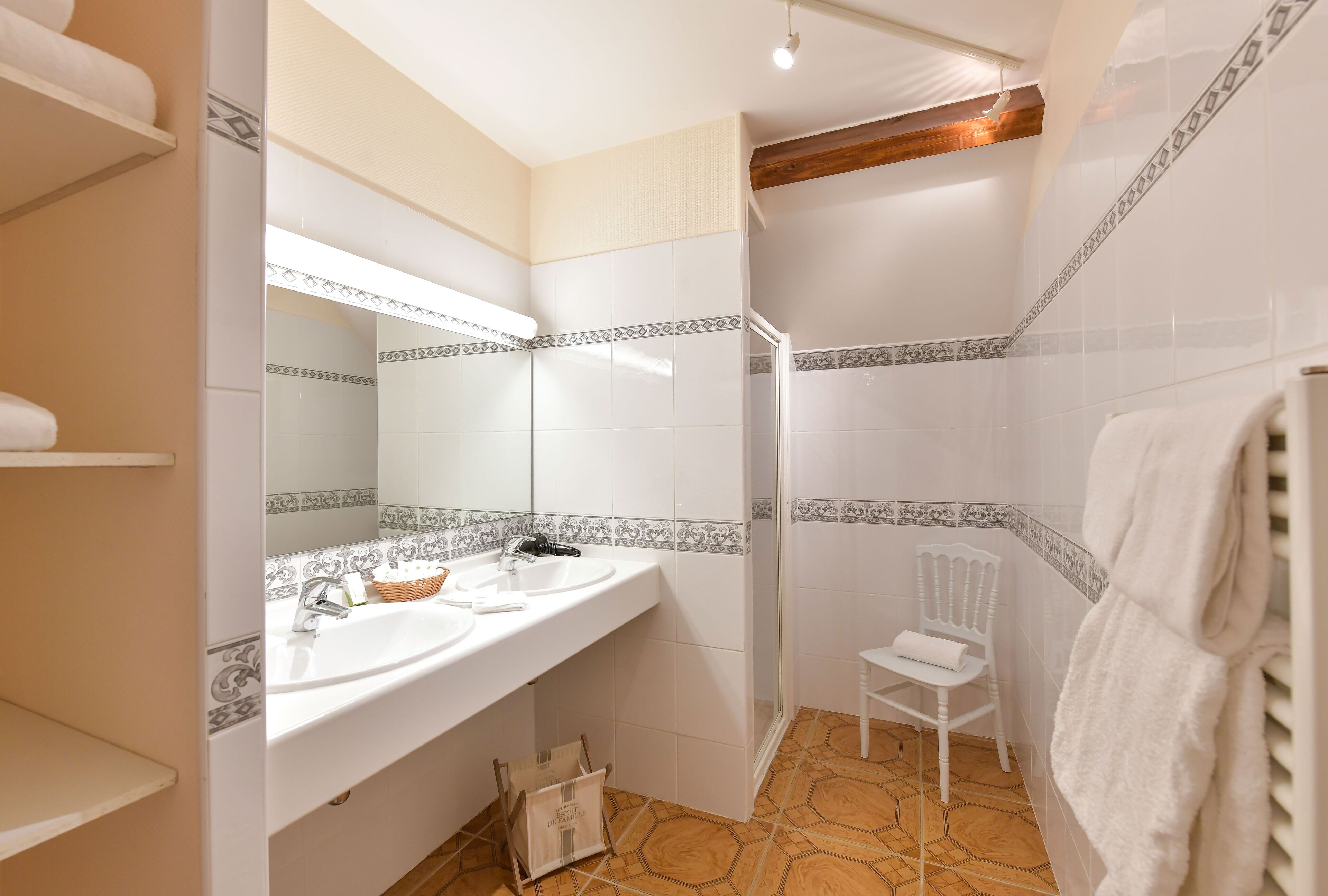 Een badkamer met twee wastafels, een spiegel, een douche en een stoel.