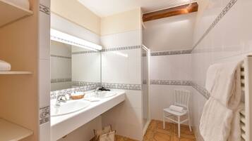 Een badkamer met twee wastafels, een spiegel, een douche en een stoel.