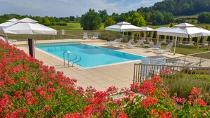 A swimming pool with sun loungers and umbrellas, surrounded by a fence and red flowers. - Le clos champagnac at Hotel Golf Chateau de Chailly (Chailly-sur-Armancon)