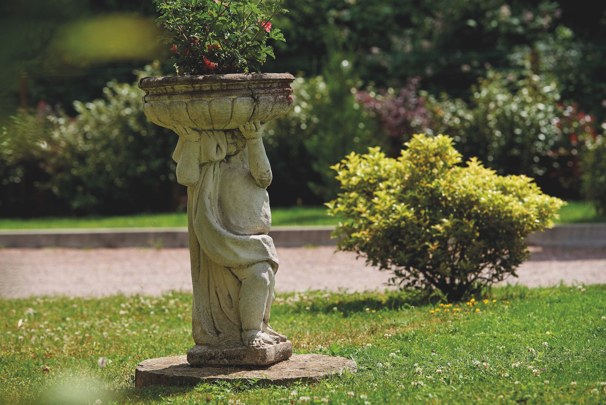 Eine Gartenstatue mit einem Blumenkasten auf einem Steinsockel.