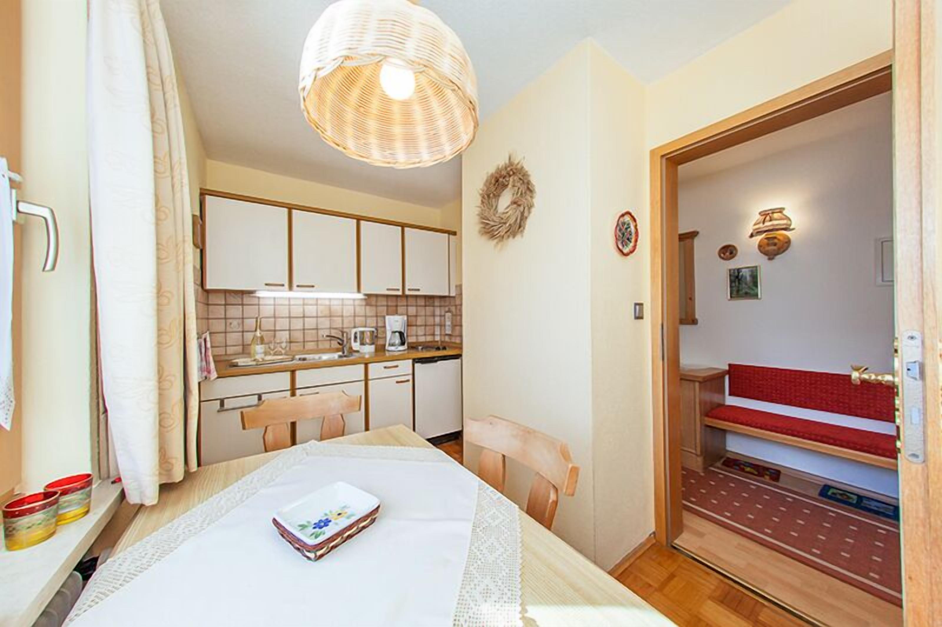 A compact kitchen with white cabinets, a dining table with a placemat, and a wicker pendant light.