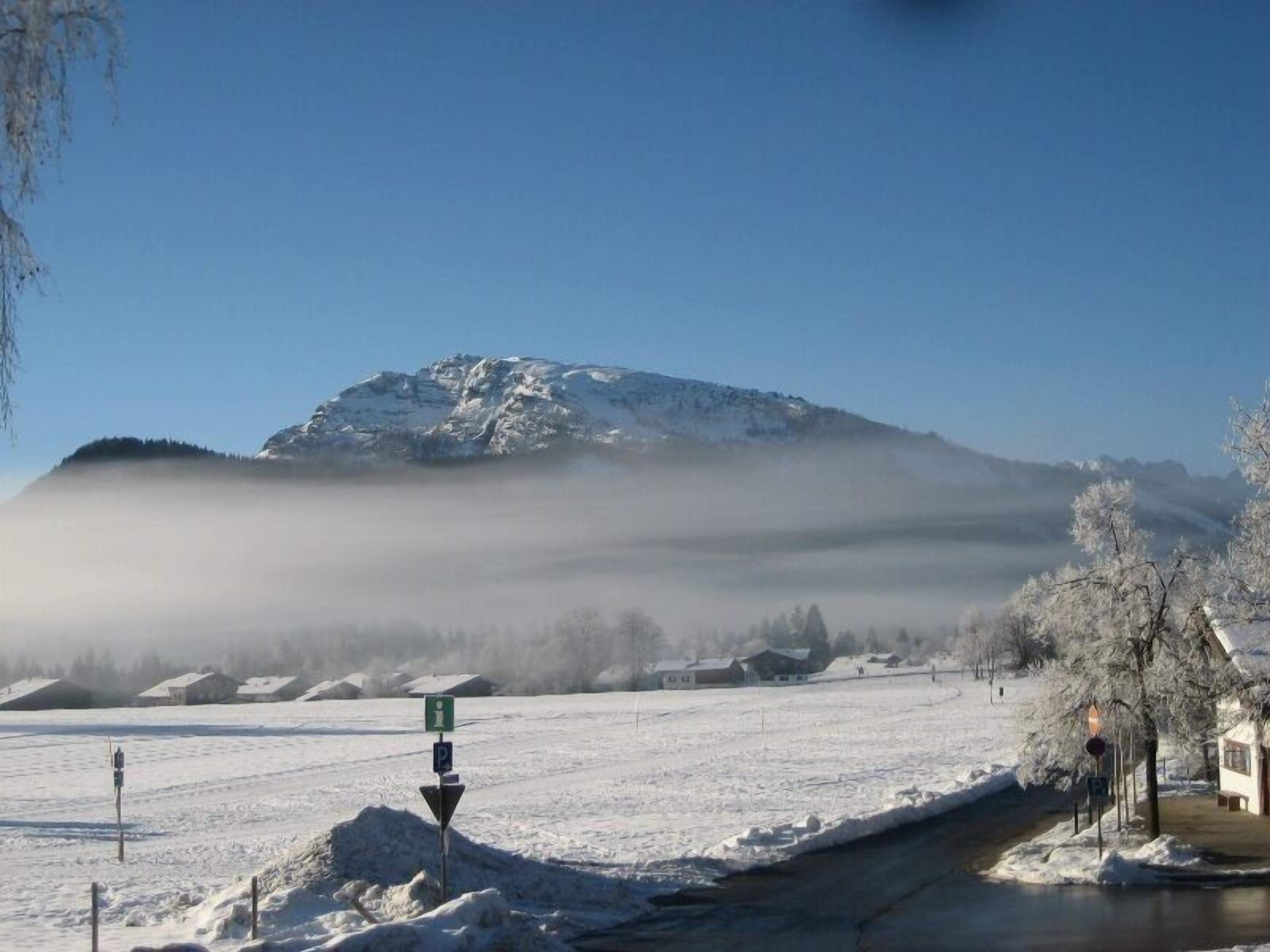 Een besneeerd landschap met een berg op de achtergrond, een heldere lucht en een gebouw met een met sneeuw bedekte dak.