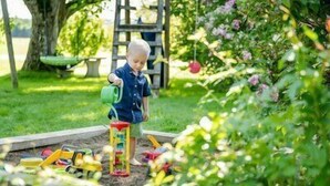 Et barn vander planter i en have med en legeplads i træ i baggrunden.