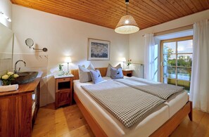 A bedroom with a large bed, bedside tables, a wooden ceiling, and a window with curtains. - Ferienwohnung "Margerite", 61 qm Obergeschoss, 2 separate Schlafzimmer (Höslwang)