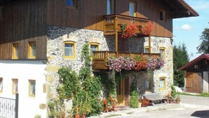 Una casa de madera de dos pisos con fachada de piedra, un balcón con cestas de flores colgantes y un pequeño porche.