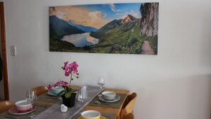 Una mesa de comedor dispuesta con platos, tazones y cubiertos, una orquídea en maceta y un cuadro de un paisaje montañoso.