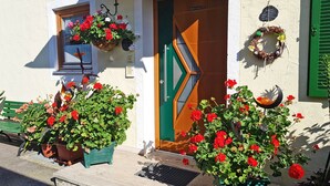 Un bâtiment avec une porte verte, une fenêtre ornée d’un pot de fleurs suspendu et une guirlande accrochée au mur.