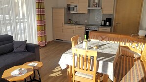 Un espace de vie compact comprenant un canapé, une table à manger avec des chaises, un coin cuisine avec des placards et des appareils électroménagers, et une fenêtre avec des rideaux.