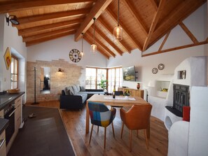 Un vaste espace de vie agrémenté de poutres en bois, d’un mur en pierre, d’un canapé, d’une table à manger avec des chaises et d’une cheminée.
