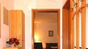 Un corridoio con pavimento in legno, un tappeto, un armadietto di legno e una porta che dà su una stanza con tavolo e sedie.