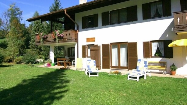 Una casa a due piani con un portico coperto, un balcone fiorito e un patio con mobili da esterno.