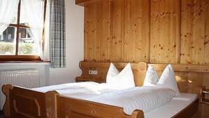 Una cama de madera con cabecera, ropa de cama blanca y una ventana con cortinas.