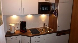 A compact kitchen with white cabinets, a built-in microwave, a coffee maker, and a sink. - Two-room apartment, 40m², bedroom and living room, kitchenette, balcony (Reit im Winkl)