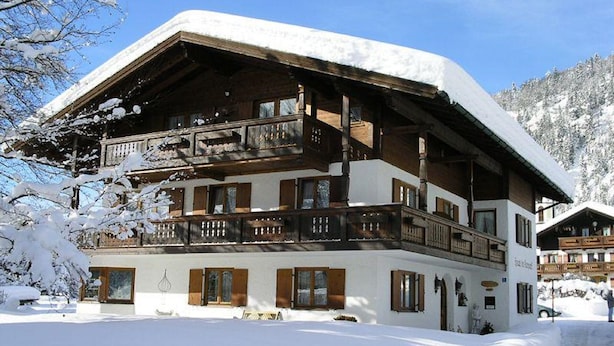 A multi-story chalet with a snow-covered roof and balconies, surrounded by a snowy landscape. - Two-room apartment, 40m², bedroom and living room, kitchenette, balcony (Reit im Winkl)