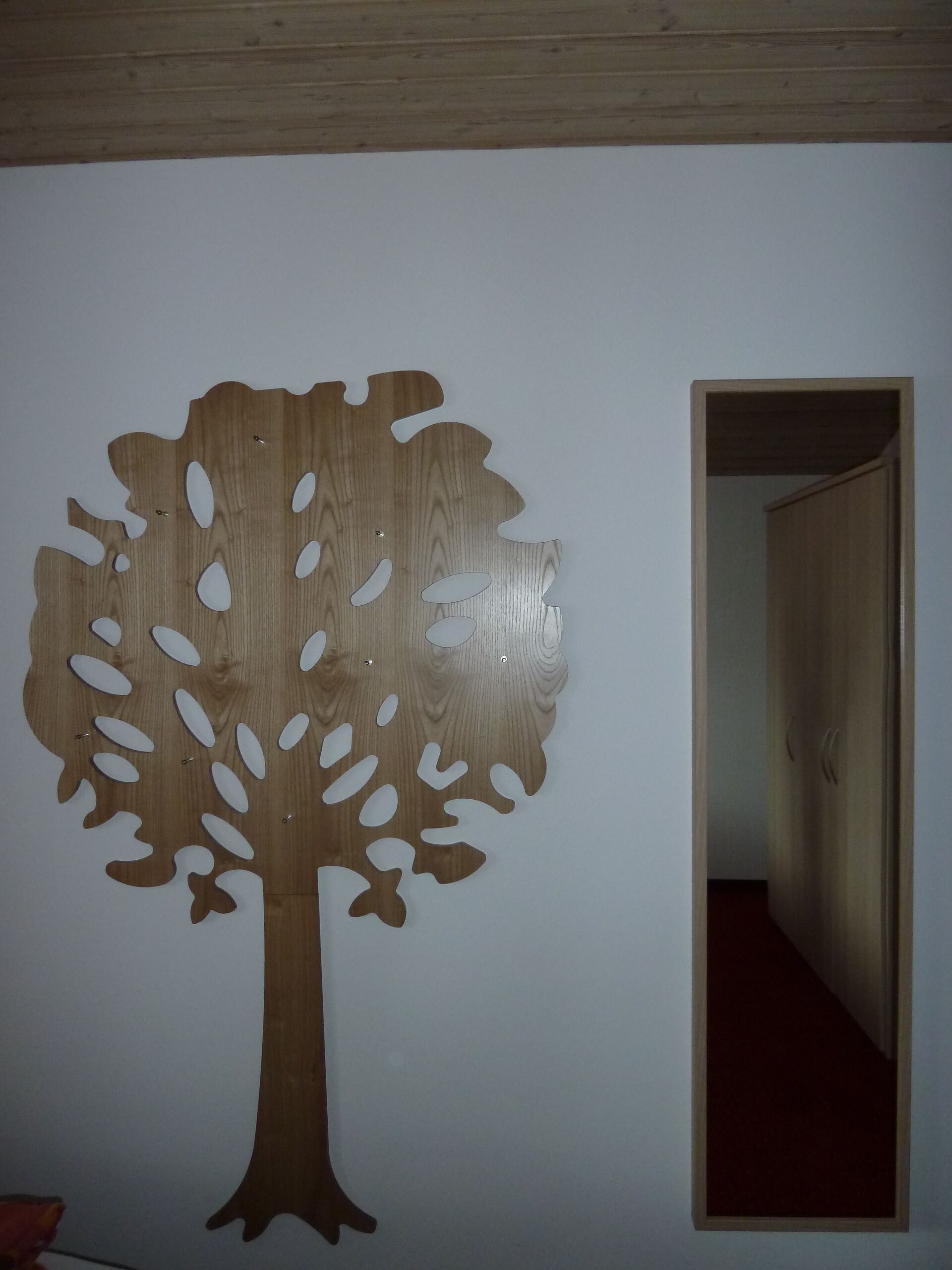 A wall with a large wooden tree cutout and a doorway leading to another room.