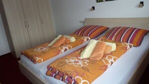 A double bed with floral and striped bedding, a wooden wardrobe, and a painting of a forest stream on the wall. - Two-room apartment, 40m², bedroom and living room, kitchenette, balcony (Reit im Winkl)