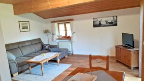 Una sala de estar acogedora con un sofá, una mesa de centro, un televisor sobre un mueble de madera y un cuadro en la pared.