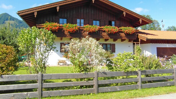 Una cabaña tradicional con techo inclinado, balcón de madera con jardineras y fachada blanca.