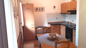 Cocina compacta con armarios de madera, una mesa de comedor con sillas, un refrigerador y un salpicadero de azulejos.