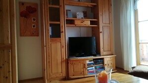 A wooden entertainment unit with a flat-screen TV, shelves, and a glass table with a drink. - Ferienwohnung 50qm, Allergikerfreundlich, Küche, Dusche/WC, Südbalkon (Reit im Winkl)