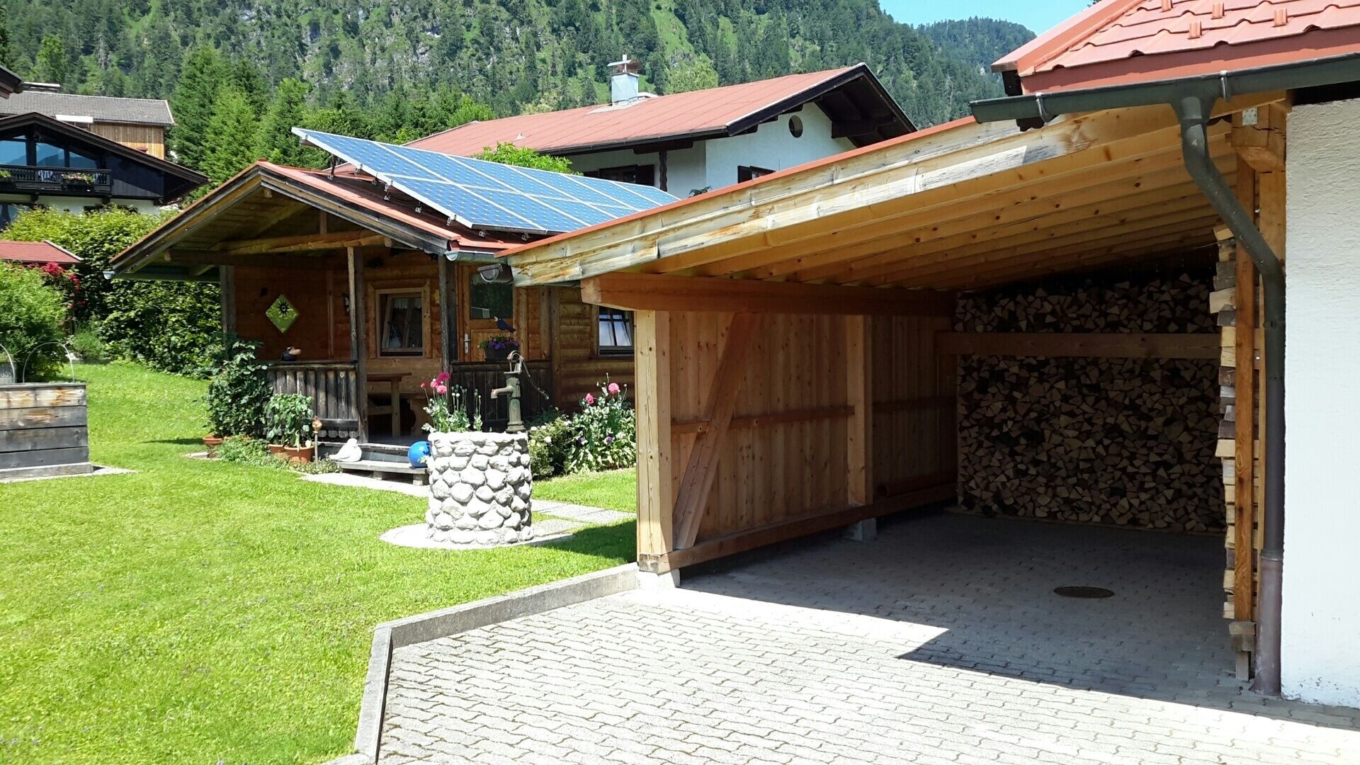 A wooden cabin with a covered porch, solar panels, and a stone well.