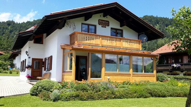 A two-story building with a wooden balcony, a sign reading "Bergidyl", and a garden with flowers in front. - Ferienwohnung 50qm, Allergikerfreundlich, Küche, Dusche/WC, Südbalkon (Reit im Winkl)