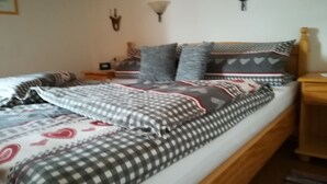 A bed with a checkered bedspread, pillows with heart patterns, and a bedside table with a lamp. - Ferienwohnung 50qm, Allergikerfreundlich, Küche, Dusche/WC, Südbalkon (Reit im Winkl)