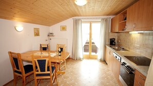A wooden-paneled kitchen with a dining table and chairs, a built-in oven, and a large window with curtains. - Ferienwohnung 50qm, Allergikerfreundlich, Küche, Dusche/WC, Südbalkon (Reit im Winkl)