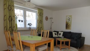 Ein Essbereich mit Holztisch und Stühlen, einem kleinen Beistelltisch, einer Couch und einem Fenster mit Vorhängen.