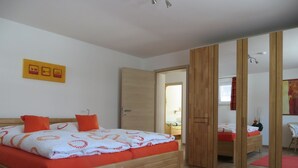 Ein Schlafzimmer mit einem hölzernen Bett, orangefarbener Bettwäsche, einem Spiegel und einem roten Teppich.