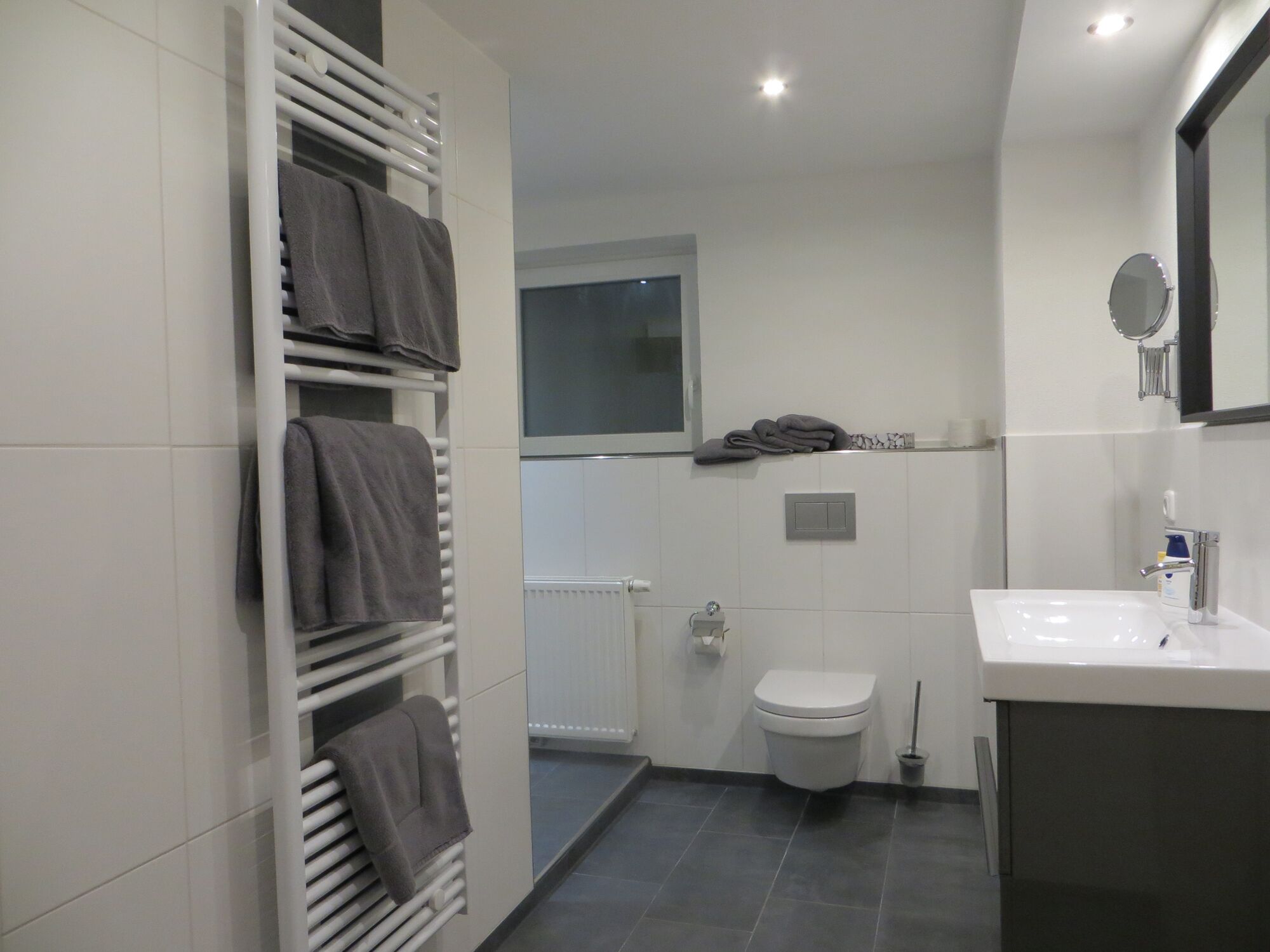 A modern bathroom with a white sink, a toilet, a towel rack with towels, and a window.