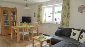 Ein Wohnzimmer mit einer Couch, einem Esstisch mit Stühlen, einem Fernseher und einer Vitrine.