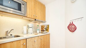 A kitchen with wooden cabinets, a stainless steel microwave, a coffee maker, and a hanging red kitchen towel. - Zwei-Raum-Ferienwohnung "Bergblick", 37m², extra Schlafzimmer, sep. Küche und Balkon (Reit im Winkl)