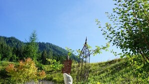 Eine rustikale Holzbrücke über einen Kiesweg mit einem Metallschild in einer Berglandschaft.