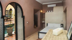A bedroom with a bed, a bedside table, a wall-mounted air conditioner, and a small window.
