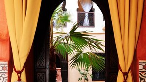 An archway with yellow curtains and tassels, leading to a pool area with a palm tree and a tiled floor.